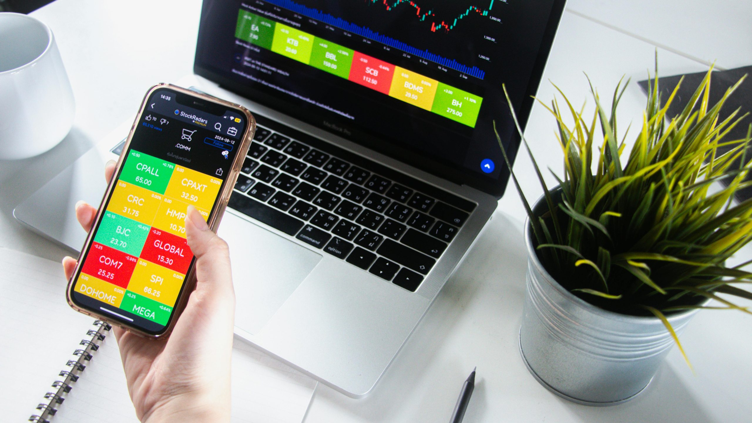 Person analyzing stock market trends on smartphone and laptop.