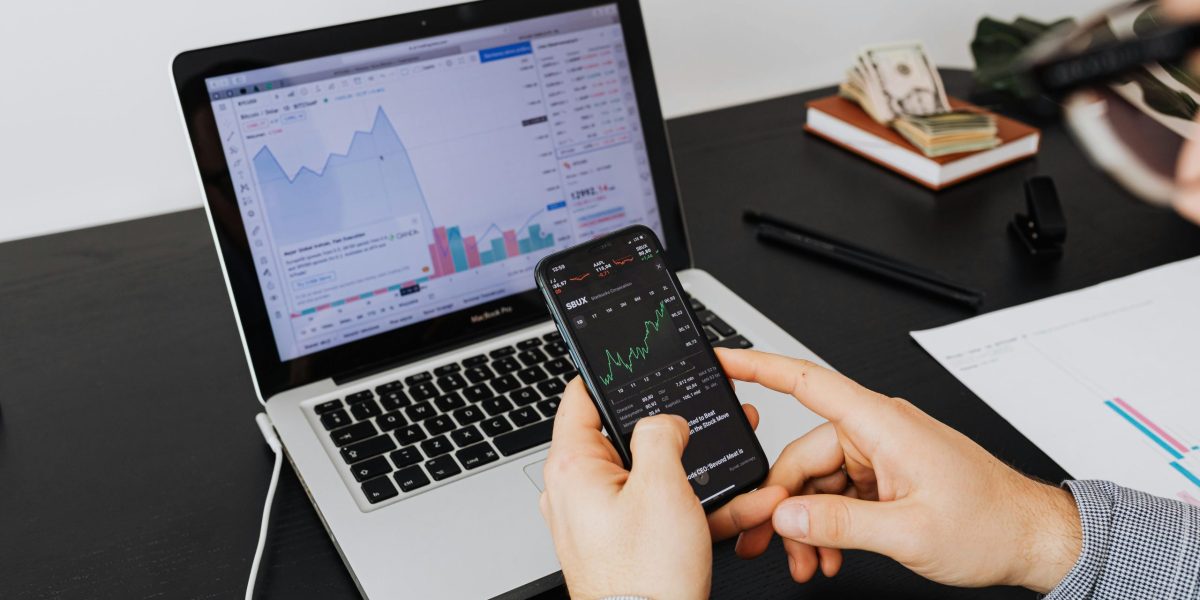 Person analyzing stock market data on a laptop and smartphone indoors.